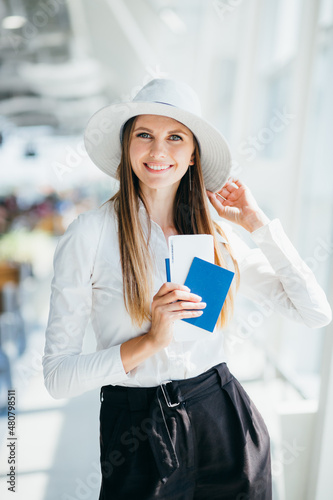 Cheerful businesswoman waiting for her flight at airport. Young woman at the airport. Young woman holding passport and boarding pass at airport. Attractive young woman going on a trip by air.