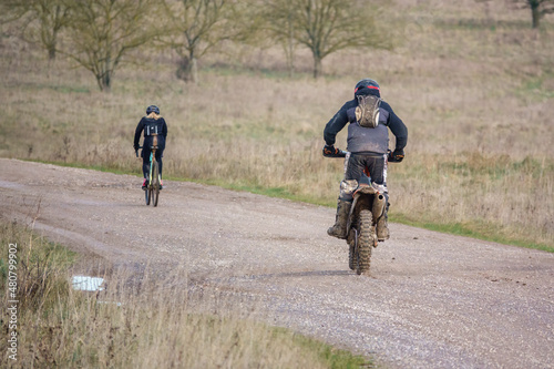 a motor cyclist (biker) riding his off-road motorbike along a stone track and overtaking pedal cyclists © Martin