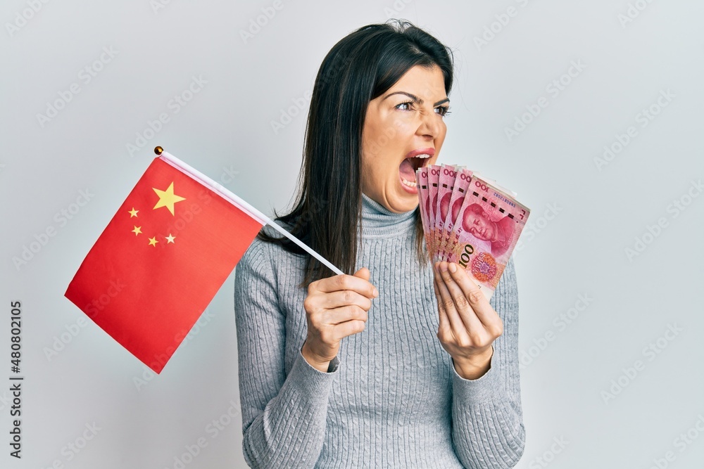 Φωτογραφία Young hispanic woman holding china flag and yuan banknotes angry and mad screaming frustrated and furious, shouting with anger