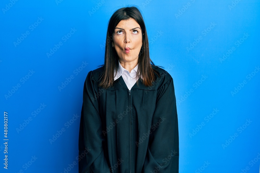 Fototapeta premium Young hispanic woman wearing judge uniform making fish face with lips, crazy and comical gesture. funny expression.