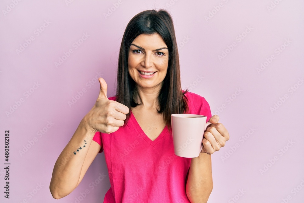 Young hispanic woman drinking a cup of coffee celebrating victory with happy smile and winner expression with raised hands Young hispanic woman drinking a cup of coffee celebrating victory with happy smile and winner expression with raised hands