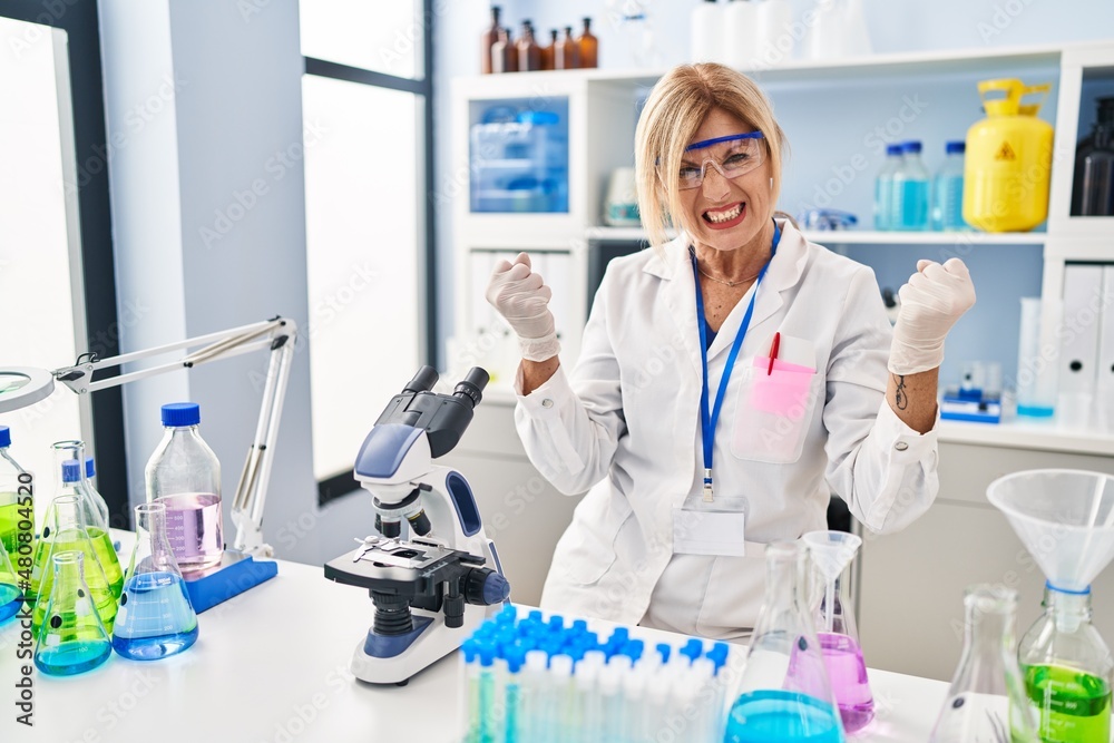 Middle age blonde woman working at scientist laboratory angry and mad raising fists frustrated and furious while shouting with anger. rage and aggressive concept. Middle age blonde woman working at scientist laboratory angry and mad raising fists frustrated and furious while shouting with anger. rage and aggressive concept.