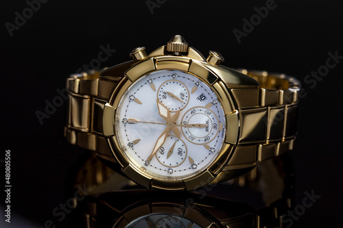 golden ladies watch with a metal bracelet, chronometer, precious stones, diamonds on a black background with reflection. The concept of an expensive gift for women, luxury. Close-up, macro
