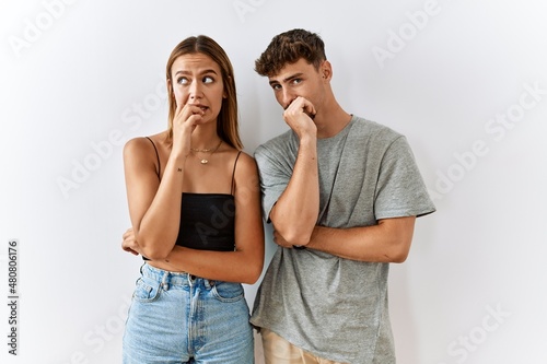 Young beautiful couple standing together over isolated background looking stressed and nervous with hands on mouth biting nails. anxiety problem.