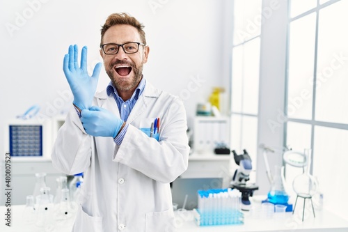 Middle age man working at scientist laboratory smiling and laughing hard out loud because funny crazy joke.