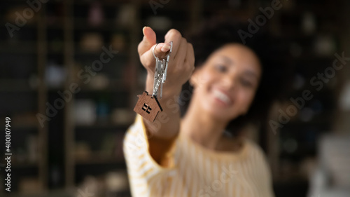 Close up focus on keys in hands of smiling young African American woman, celebrating moving into rental apartment. Sincere happy female homeowner purchasing first dwelling, real estate, tenancy.