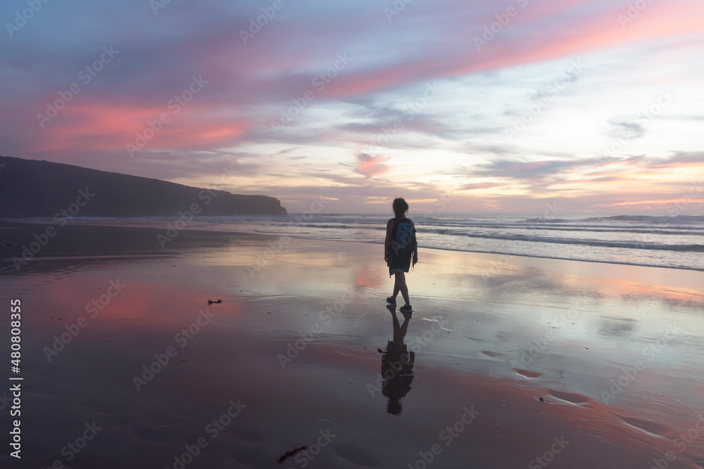 Woman walking at sunset along Malhão beach