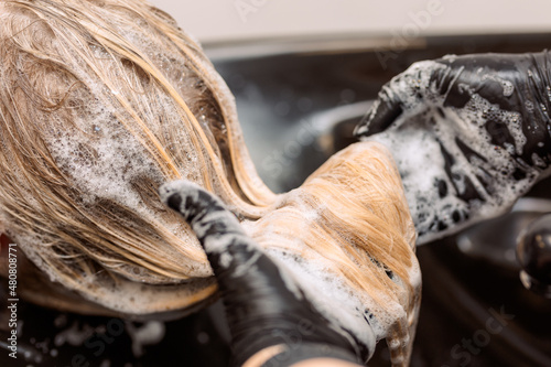 close-up. hairdresser in black rubber gloves washes hair to a client after dyeing