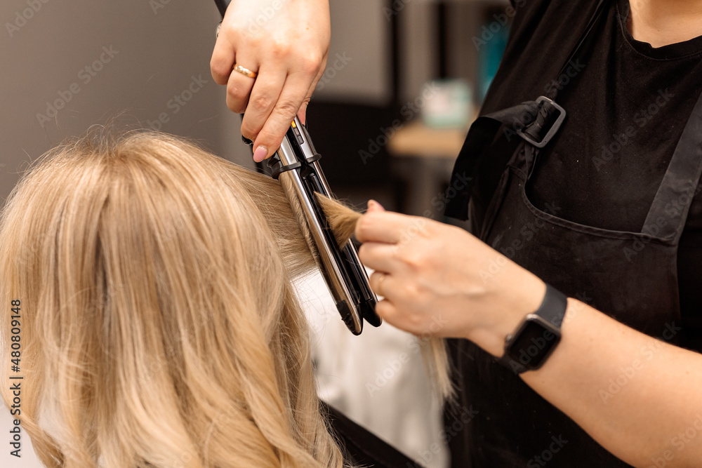 Φωτογραφία The hairdresser curls the hair of the client with a hair straightener