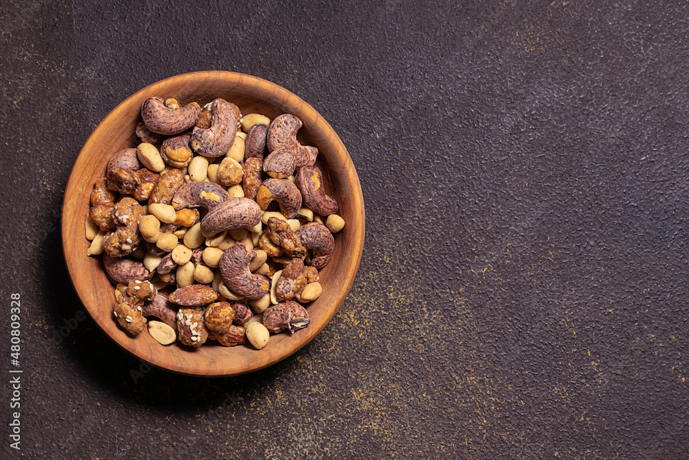 Assortment of tasty organic nuts in the wooden bowl on dark rustic background. Copy space for your text. Assortment of tasty organic nuts in the wooden bowl on dark rustic background. Copy space for your text.