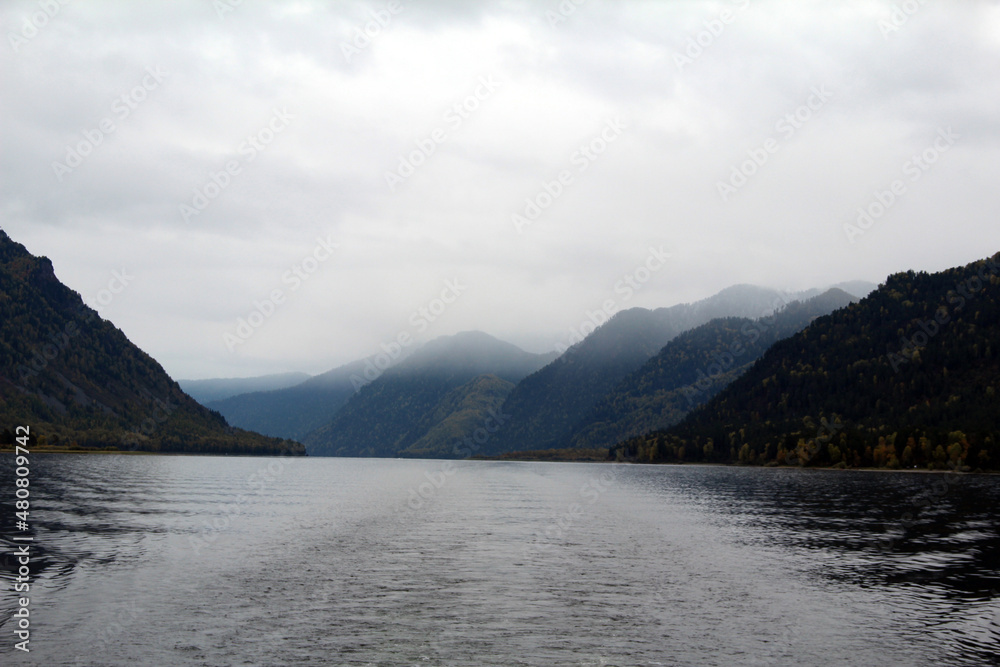 Autumn foggy landscape in Altai. A trace of a passing ship in Lake Teletskoye. Mountains in the fog.
