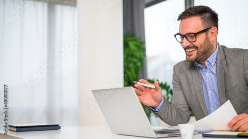 Smiling attractive young manager with a stylish short beard talking online with his clients discussing a business proposal