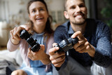 Happy laughing young family couple gamers using remote controller, playing virtual reality entertaining video games, having fun together at home, enjoying carefree leisure hobby weekend time.