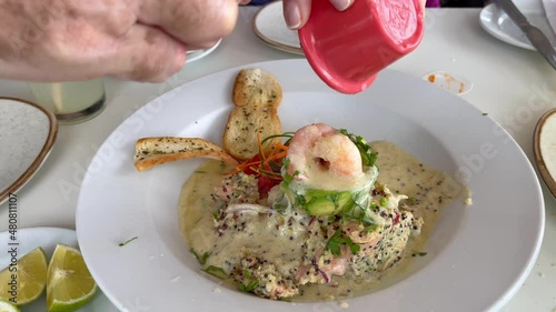 Hand pouring tiger milk on salmon quinoa ceviche with avocado and prawns on top. Mixing of traditional gourmet food from Peru