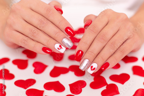 Beautiful female hands with romantic manicure nails, red gel polish, hearts and Valentine's day design