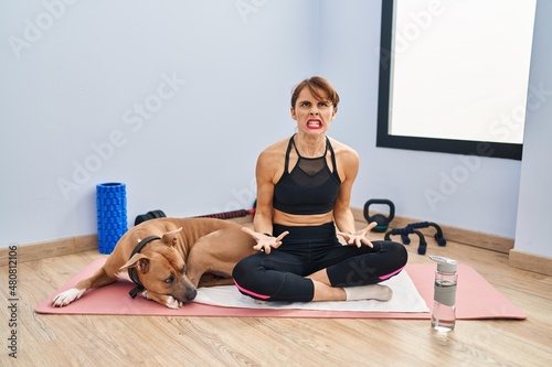 Young beautiful woman sitting on yoga mat angry and mad screaming frustrated and furious, shouting with anger. rage and aggressive concept.