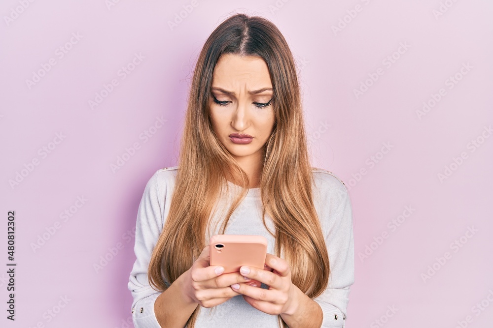 Young blonde girl using smartphone typing message skeptic and nervous, frowning upset because of problem. negative person. Young blonde girl using smartphone typing message skeptic and nervous, frowning upset because of problem. negative person.