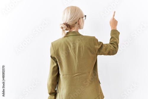 Beautiful caucasian business woman standing over isolated background posing backwards pointing ahead with finger hand photo