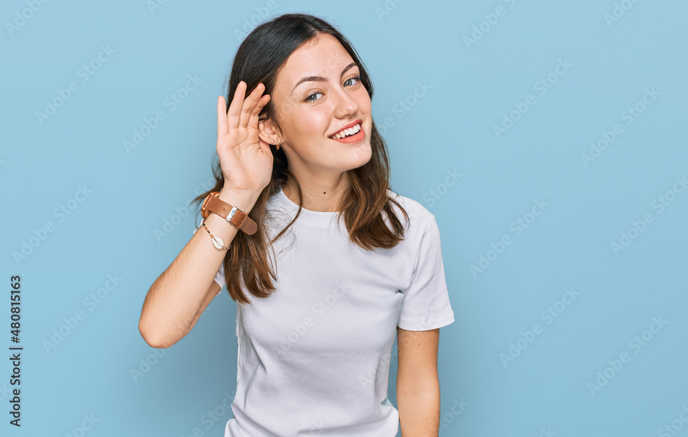 Young beautiful woman wearing casual white t shirt smiling with hand over ear listening an hearing to rumor or gossip. deafness concept. Young beautiful woman wearing casual white t shirt smiling with hand over ear listening an hearing to rumor or gossip. deafness concept.