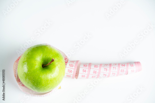 a whole green apple on a white background with a meter (measuring tape)