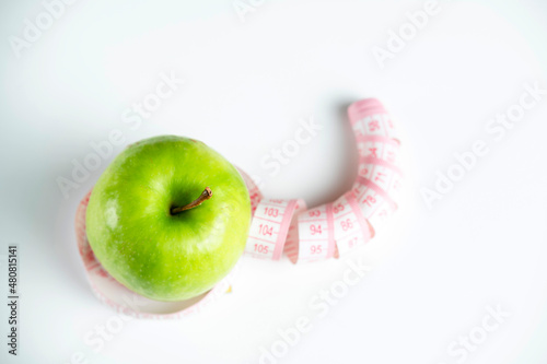 a whole green apple on a white background with a meter (measuring tape)