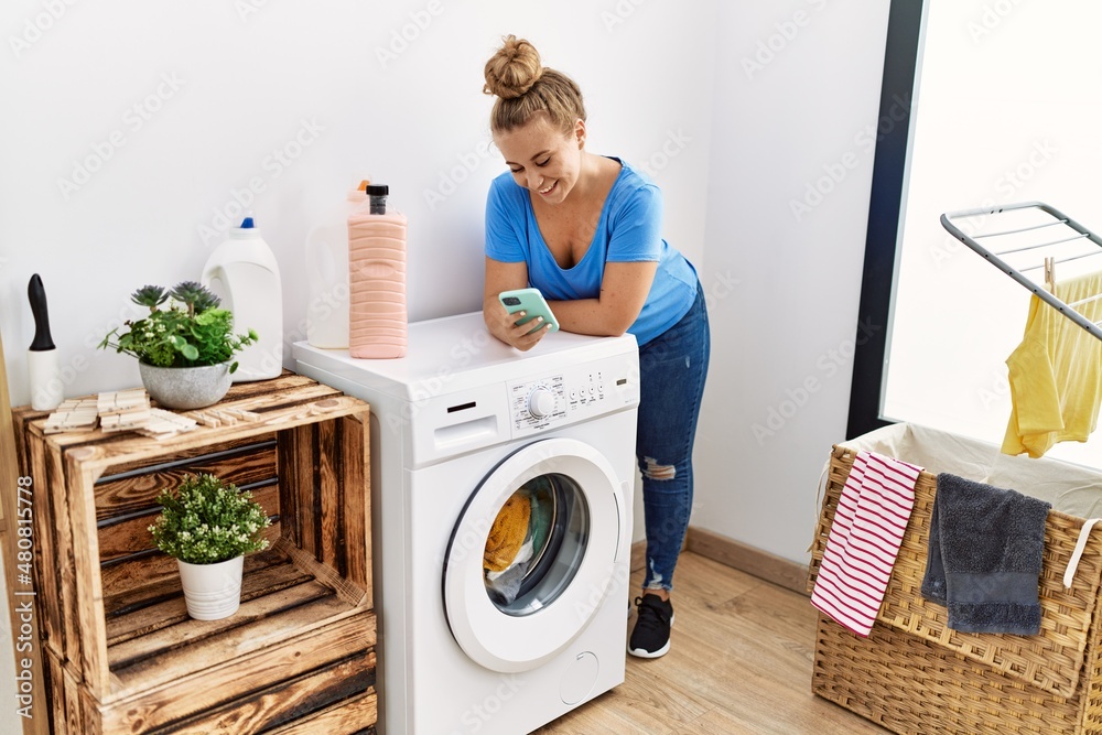 Young blonde girl using smartphone waiting for washing machine at laundry room Young blonde girl using smartphone waiting for washing machine at laundry room