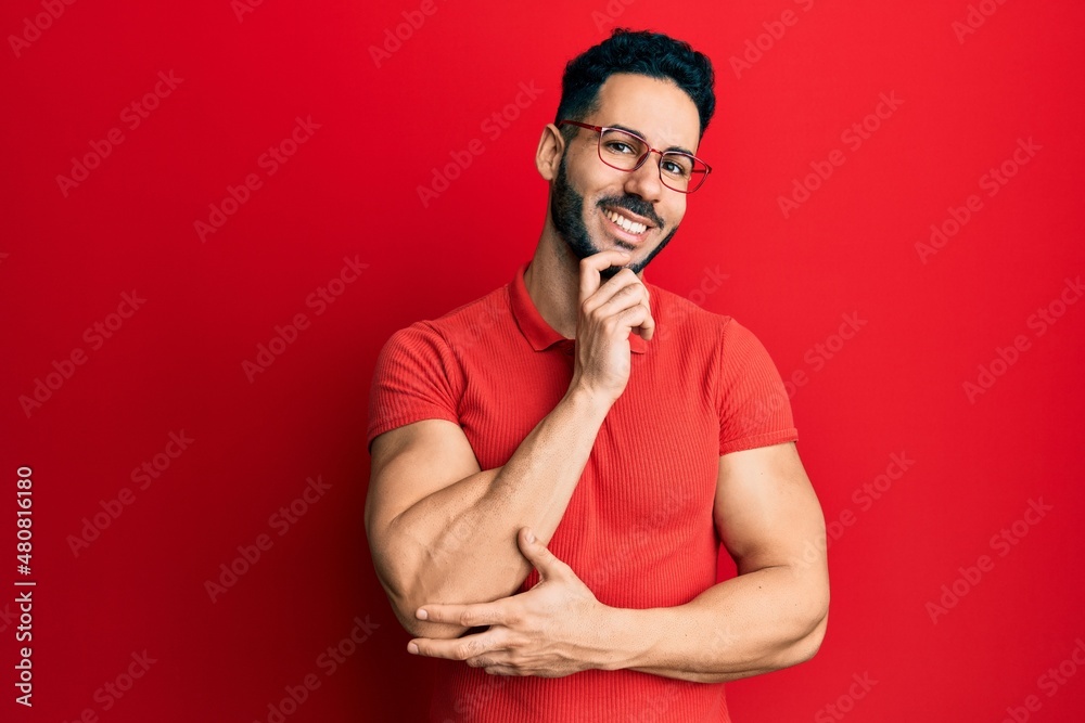 Young hispanic man wearing casual clothes and glasses looking confident at the camera with smile with crossed arms and hand raised on chin. thinking positive. Young hispanic man wearing casual clothes and glasses looking confident at the camera with smile with crossed arms and hand raised on chin. thinking positive.