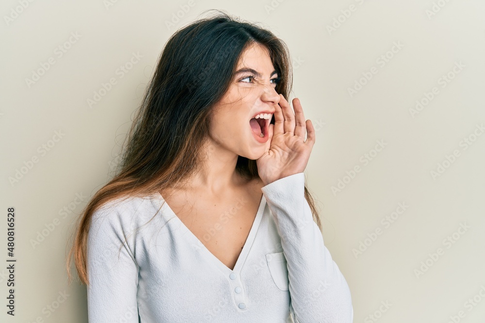 Young caucasian woman wearing casual white t shirt shouting and screaming loud to side with hand on mouth. communication concept. Young caucasian woman wearing casual white t shirt shouting and screaming loud to side with hand on mouth. communication concept.