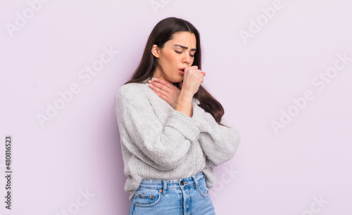 pretty young woman feeling ill with a sore throat and flu symptoms, coughing with mouth covered