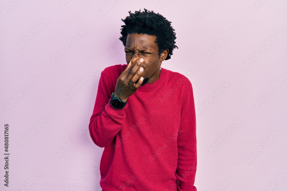 Young african american man wearing casual clothes smelling something stinky and disgusting, intolerable smell, holding breath with fingers on nose. bad smell