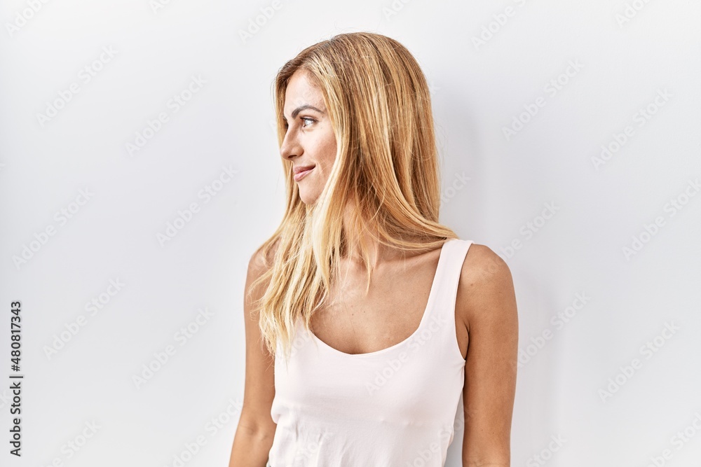 Blonde beautiful young woman standing over white isolated background looking to side, relax profile pose with natural face with confident smile. Blonde beautiful young woman standing over white isolated background looking to side, relax profile pose with natural face with confident smile.