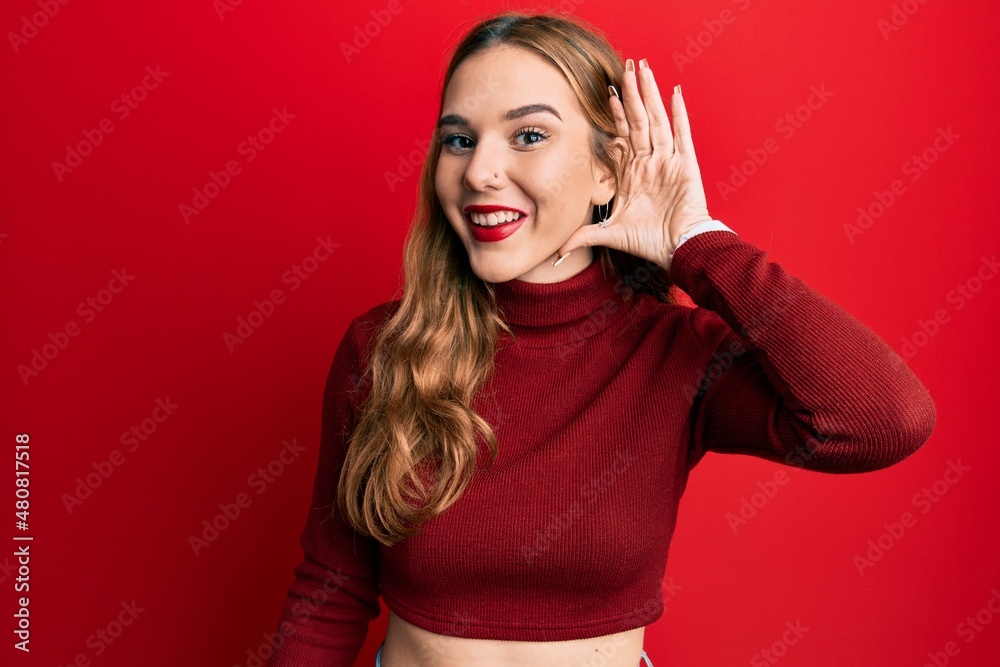 Young blonde woman wearing turtleneck sweater smiling with hand over ear listening an hearing to rumor or gossip. deafness concept. Young blonde woman wearing turtleneck sweater smiling with hand over ear listening an hearing to rumor or gossip. deafness concept.