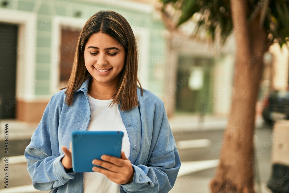 Young latin girl smiling happy using touchpad at the city.