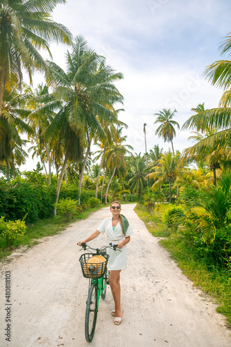 An elegant happy woman in a white dress rides a bicycle around La Digue island in the Seychelles. Happy lifestyle on summer tropical vacation