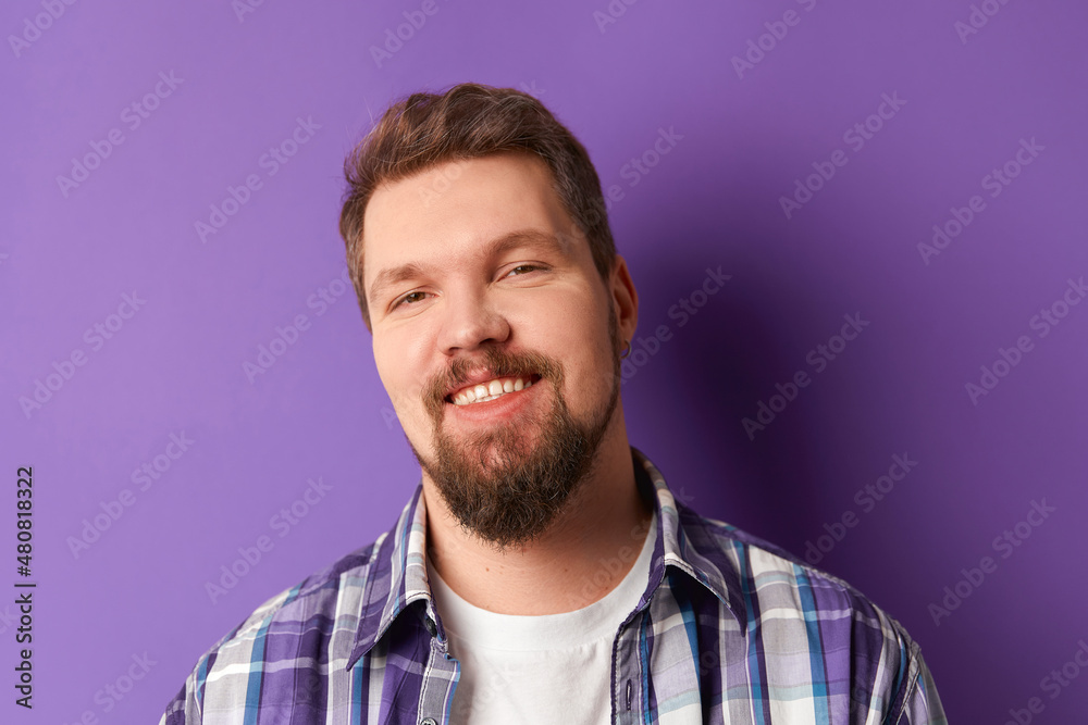 Fototapeta premium Happy bearded man in shirt smiling looking at camera on purple background. Young handsome stylish guy