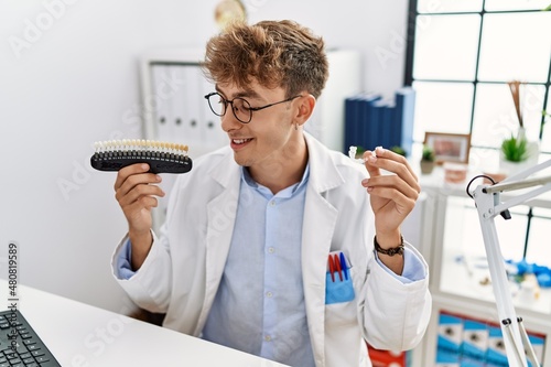 Young caucasian man wearing dentist uniform holding whitening and invisible aligner at clinic photo