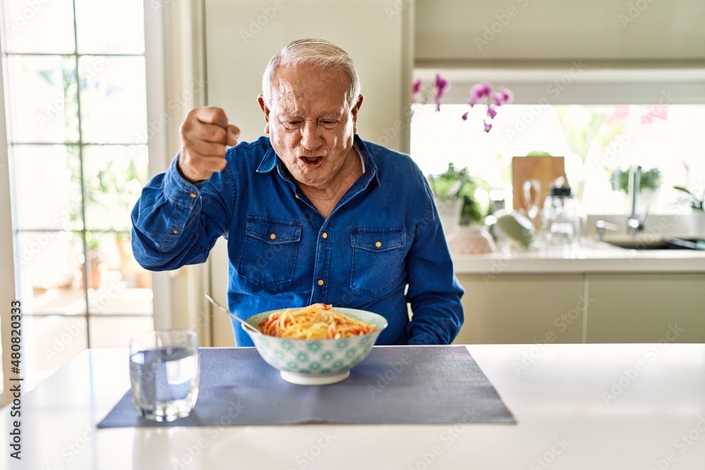 Senior man with grey hair eating pasta spaghetti at home angry and mad  raising fist frustrated and furious while shouting with anger. rage and  aggressive concept. Stock Photo | Adobe Stock