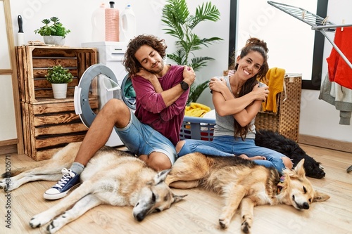 Young hispanic couple doing laundry with dogs hugging oneself happy and positive  smiling confident. self love and self care