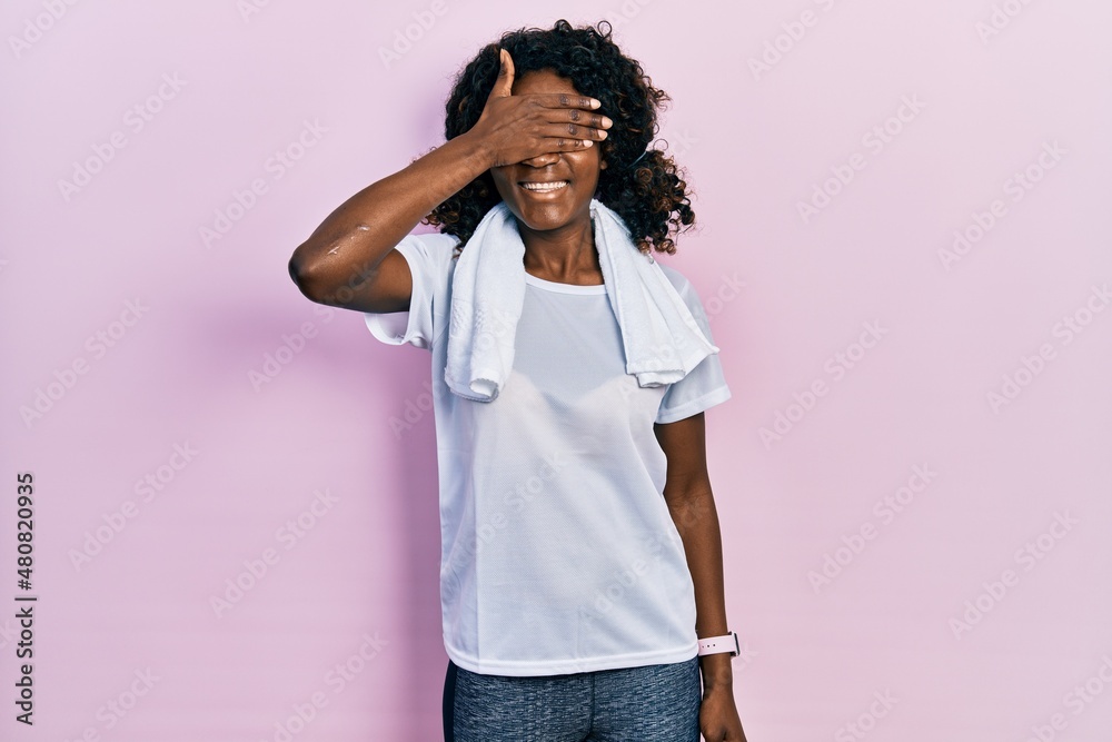 Young african american woman wearing sportswear and towel smiling and laughing with hand on face covering eyes for surprise. blind concept. Young african american woman wearing sportswear and towel smiling and laughing with hand on face covering eyes for surprise. blind concept.