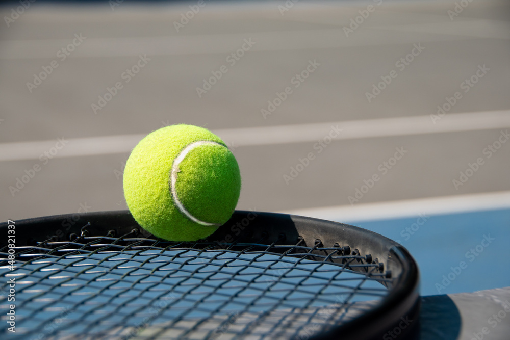 tennis ball on black racquet, on hard court