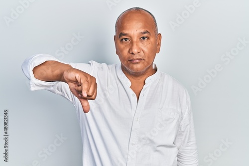 Middle age latin man wearing casual clothes looking unhappy and angry showing rejection and negative with thumbs down gesture. bad expression.