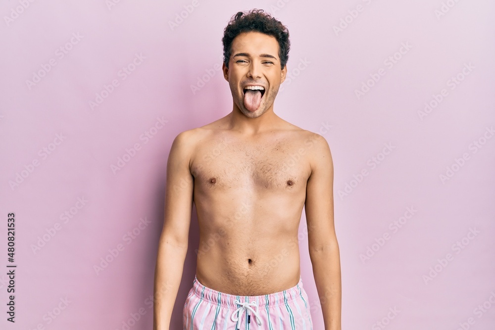 Fototapeta premium Young handsome man wearing swimwear shirtless sticking tongue out happy with funny expression. emotion concept.
