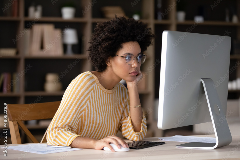 Thoughtful young African American business woman looking at computer monitor, feeling exhausted working on difficult tasks, considering project problem solution, analyzing data preparing document.