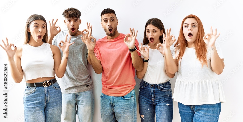 Group of young friends standing together over isolated background looking surprised and shocked doing ok approval symbol with fingers. crazy expression Group of young friends standing together over isolated background looking surprised and shocked doing ok approval symbol with fingers. crazy expression