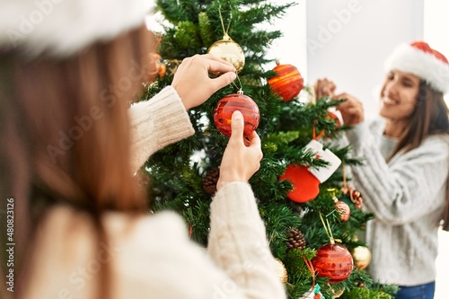 Two women smiling confident decorating christmas tree at home