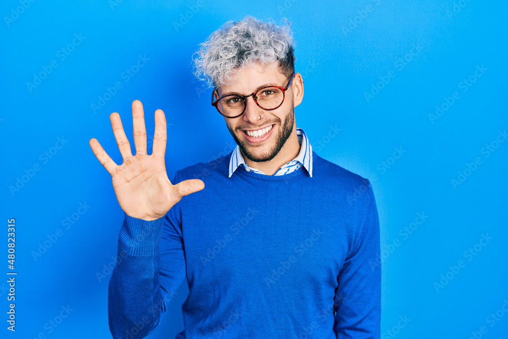 Young hispanic man with modern dyed hair wearing sweater and glasses showing and pointing up with fingers number five while smiling confident and happy. Young hispanic man with modern dyed hair wearing sweater and glasses showing and pointing up with fingers number five while smiling confident and happy.