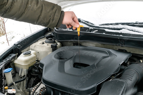 Close-up side view of auto mechanic man checking engine oil level in car, workshop, garage. car repairing service with open hood,outside backyard in winter