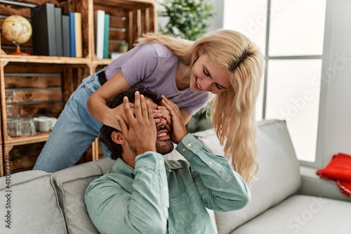 Woman surprising her boyfriend with hands on eyes at home.
