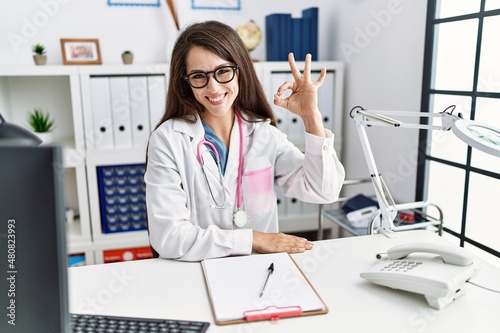 Young doctor woman wearing doctor uniform and stethoscope at the clinic smiling positive doing ok sign with hand and fingers. successful expression.