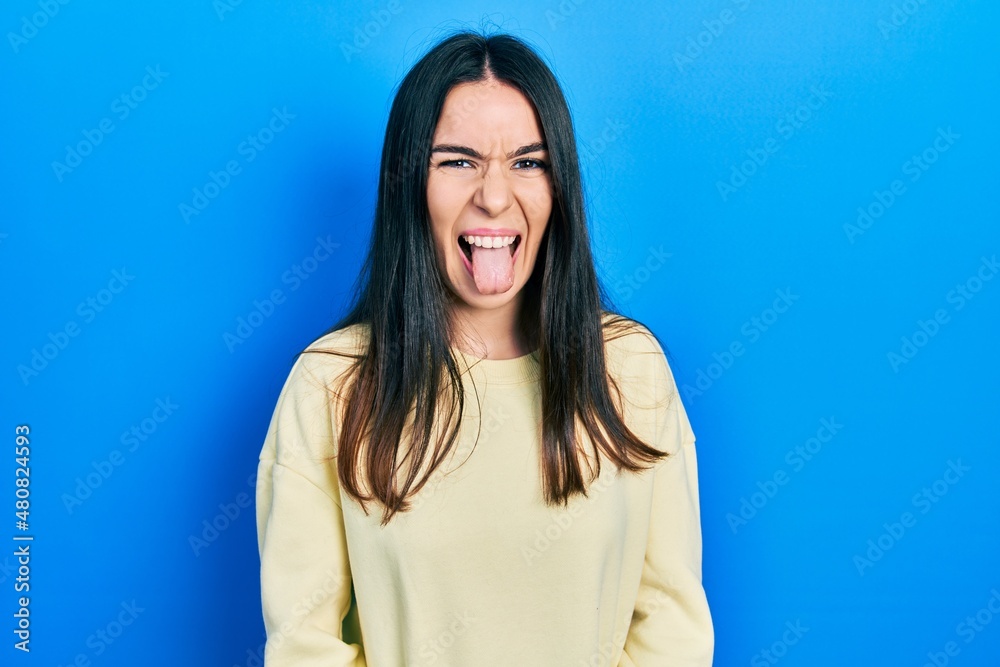 Young brunette woman wearing casual sweatshirt sticking tongue out happy with funny expression. emotion concept. Young brunette woman wearing casual sweatshirt sticking tongue out happy with funny expression. emotion concept.